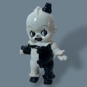 Puede incluir: Figura de payaso de cerámica vintage en blanco y negro. El payaso tiene un sombrero negro, un cuello con volantes y un atuendo bicolor. La figura tiene un acabado brillante y está de pie con los brazos ligeramente extendidos.