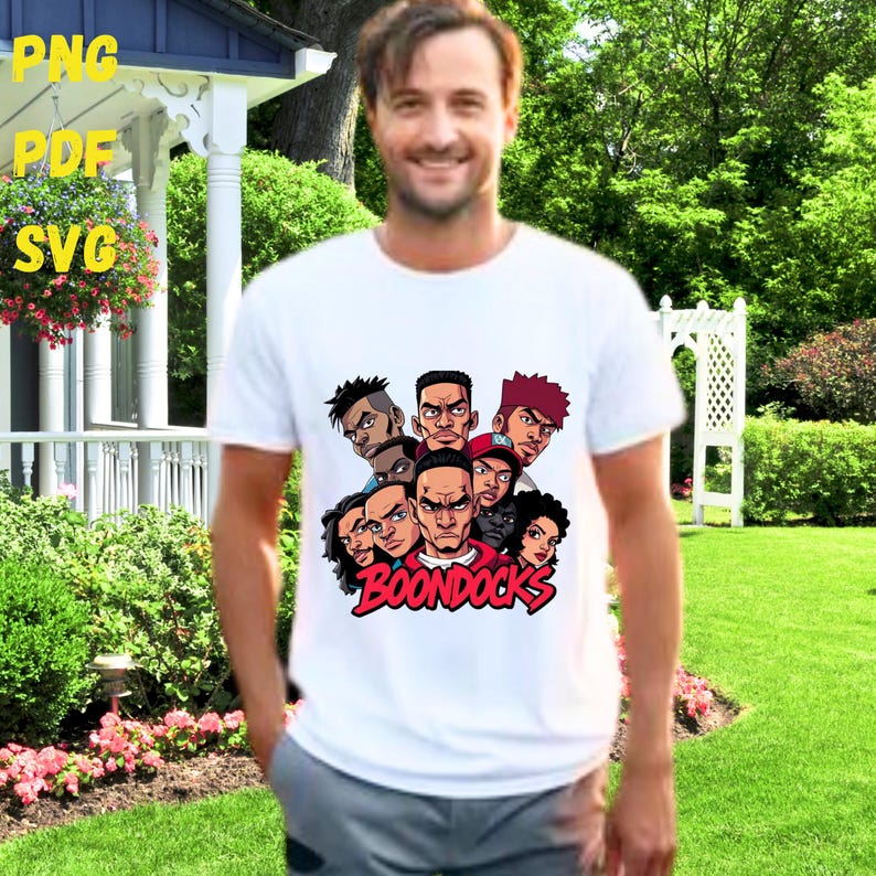 May include: White t-shirt featuring a graphic of several cartoon faces with the word "BOONDOCKS" in red. The image is of a person wearing the shirt outdoors.