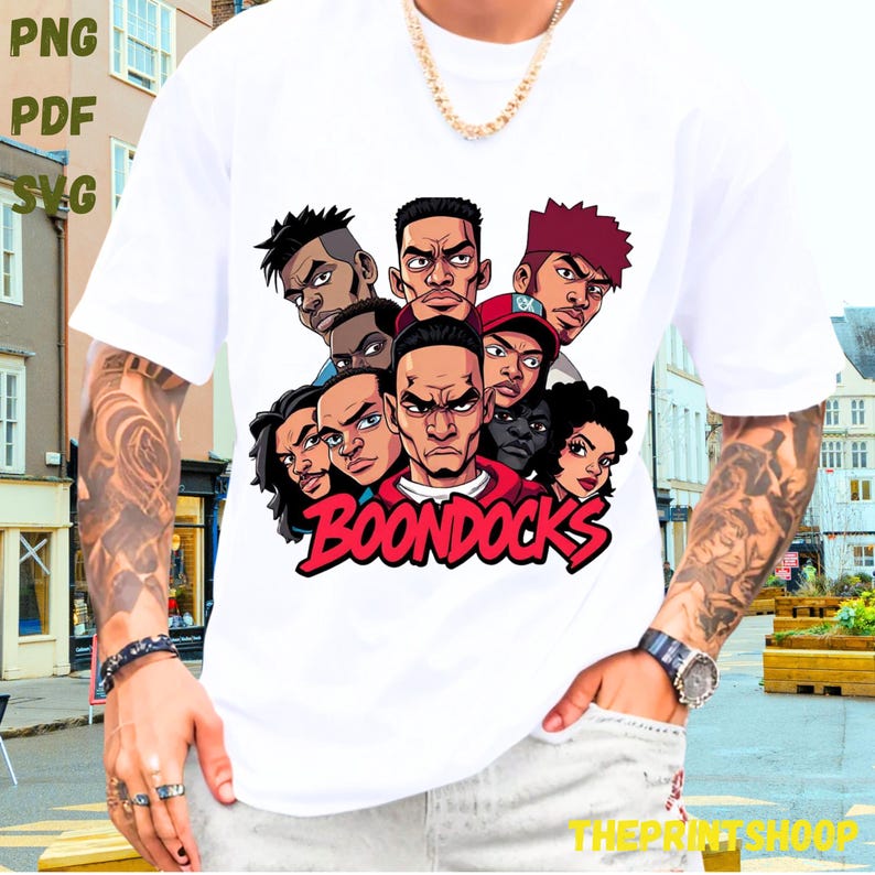 May include: White t-shirt featuring a graphic of several cartoon faces with the word "BOONDOCKS" in red. The design includes various skin tones and hairstyles. The shirt has short sleeves.