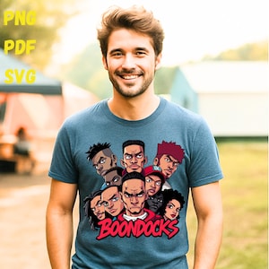 May include: A blue t-shirt featuring a graphic of several cartoon faces with the word "BOONDOCKS" in red and white. The shirt has short sleeves and is being worn by a person.