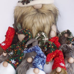 May include: A collection of handmade gnome figurines. The gnomes have long, shaggy beards, round wooden noses, and colorful, pointed hats. The hats are patterned with snowflakes, plaid, and floral designs. The main gnome has a cream-colored hat and a long, faux fur beard.