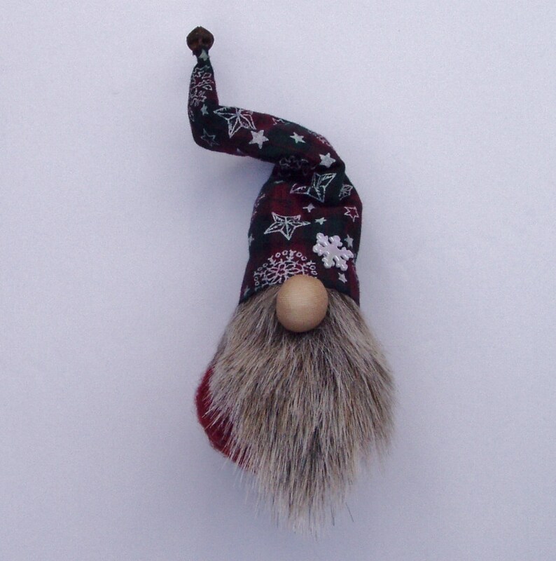 May include: A whimsical gnome figurine with a long, gray faux fur beard and a wooden nose. The hat is patterned with white stars and snowflakes on a dark red and black plaid background. The hat has a curved shape and a small brown knob at the tip.