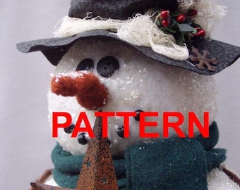 May include: A snowman figure wearing a black top hat with white fiber trim, red berries, and a small metal star. The snowman has a textured white surface, black button eyes, and a rust-colored nose. Text reads: PATTERN Happy Valley Primitives PDF Pattern Not a finished tree topper.