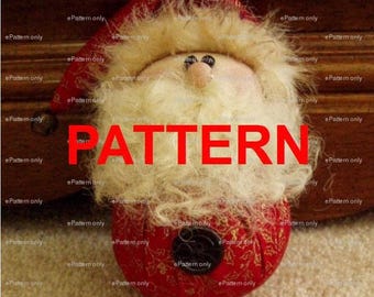 May include: A fabric Santa Claus ornament featuring a red hat with a gold leaf pattern, a fluffy cream-colored beard, a round nose, and a red body with a black button centered on the front. The word PATTERN is printed in large red letters.