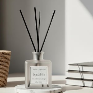 May include: A frosted glass diffuser bottle with black reeds, labeled "Coastal Gin." The bottle sits on a marble coaster, next to a woven basket and a stack of books. The overall aesthetic is minimalist and spa-like.