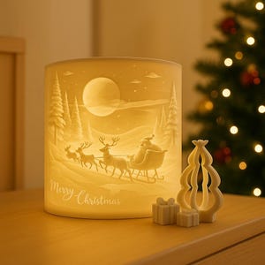 Könnte beinhalten: Ein zylindrischer, cremefarbener Weihnachtskerzenhalter mit einer Reliefszene von Santa Claus in einem von Rentieren gezogenen Schlitten, mit dem Schriftzug "Merry Christmas". Ein kleiner Weihnachtsbaum und Geschenkboxen sind ebenfalls vorhanden.