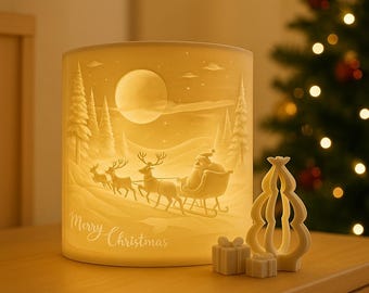 May include: A cylindrical, off-white Christmas candle holder with a relief scene of Santa Claus in a sleigh pulled by reindeer, with the words "Merry Christmas". A small Christmas tree and gift boxes are also present.