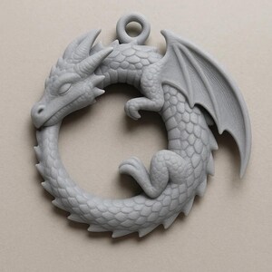 May include: A gray dragon pendant in a circular design, with the dragon biting its own tail. The pendant features detailed scales, wings, and a loop for hanging. The dragon is a mythical creature, often associated with fantasy and medieval themes.