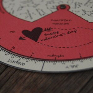 K&ouml;nnte beinhalten: Ein roter und wei&szlig;er runder Kalender mit einem schwarzen Herz- und Pfeilmotiv. Der Kalender hat eine schwarze Aufschrift mit der Aufschrift "Happy Valentine's Day!" und eine schwarze Aufschrift mit der Aufschrift "Southern Horizon". Der Kalender hat eine schwarze Aufschrift mit der Aufschrift "August" und eine schwarze Aufschrift mit der Aufschrift "July".