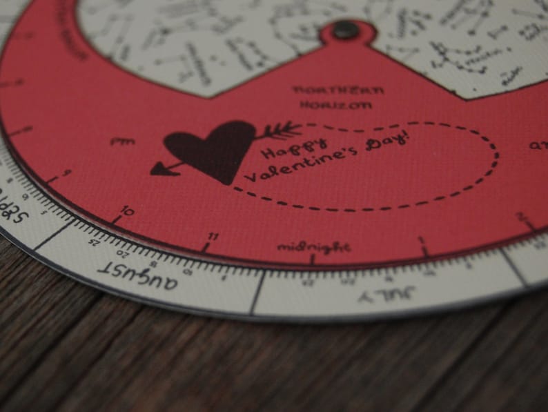 K&ouml;nnte beinhalten: Ein roter und wei&szlig;er runder Kalender mit einem schwarzen Herz- und Pfeilmotiv. Der Kalender hat eine schwarze Aufschrift mit der Aufschrift "Happy Valentine's Day!" und eine schwarze Aufschrift mit der Aufschrift "Southern Horizon". Der Kalender hat eine schwarze Aufschrift mit der Aufschrift "August" und eine schwarze Aufschrift mit der Aufschrift "July".