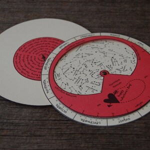 K&ouml;nnte beinhalten: Eine rote und wei&szlig;e Sternenkarte aus Papier mit einer Herzform und dem Text "Happy Valentine's Day". Die Karte ist ein kreisf&ouml;rmiges Rad mit einem kleineren wei&szlig;en Kreis in der Mitte. Die Karte zeigt die Sternbilder des Nachthimmels.
