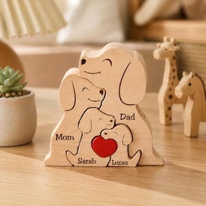 Könnte beinhalten: Ein helles Holzpuzzle mit vier ineinandergreifenden Hundefiguren. Die Figuren sind mit den Namen Mom, Dad, Sarah und Lucas graviert. Ein kleines, rotes Herz befindet sich zwischen den beiden kleineren Hundefiguren in der Mitte.