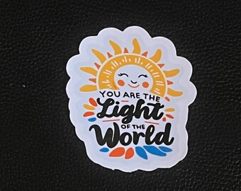 May include: A white sticker featuring a yellow sun with a smiling face and the text "You are the light of the world" in colourful lettering.
