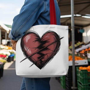 Puede incluir: Bolso tote blanco con un diseño de corazón rojo desgastado con una línea negra. El bolso tiene correas rojas y se lleva al hombro. El fondo muestra un mercado con productos.