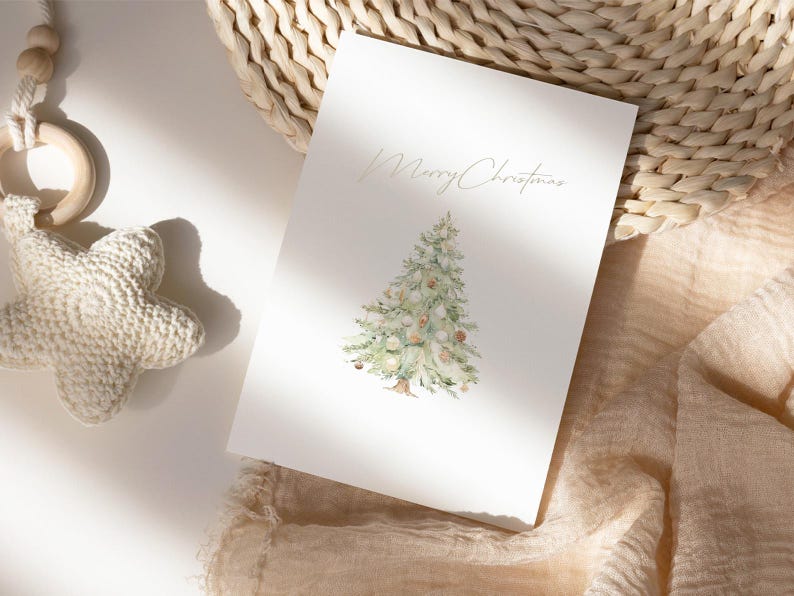 Pode incluir: Um cart&atilde;o de felicita&ccedil;&otilde;es branco com um desenho de &aacute;rvore de Natal em aquarela e a frase "Merry Christmas". O cart&atilde;o est&aacute; sobre uma superf&iacute;cie neutra com uma cesta tecida e um brinquedo em forma de estrela.