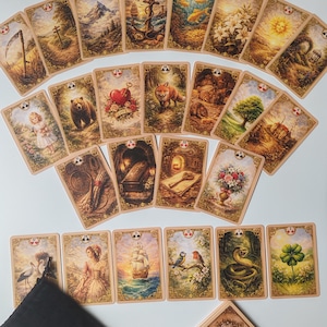Puede incluir: Un conjunto de cartas de tarot con ilustraciones variadas, incluyendo una cruz, un ancla, un zorro y un oso. Las cartas están dispuestas en abanico, con una bolsa de terciopelo negro y una baraja de cartas en la esquina inferior derecha.