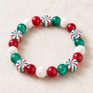 May include: A circular stretch bracelet featuring alternating beads in red, green, and white. The design includes translucent red and green spheres, opaque white faceted beads, and cylindrical beads with a red, white, and green swirl pattern.