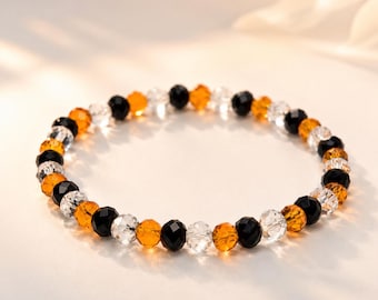 Puede incluir: Una pulsera de cuentas con un patrón repetitivo de cuentas redondas facetadas en colores transparente, negro y naranja. Las cuentas están ensartadas en un cordón elástico, creando una forma circular con un acabado pulido y reflectante.