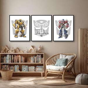 May include: Three framed art prints featuring Transformers characters. One print shows Bumblebee in yellow and black, another has the name "Jayden", and the third depicts Optimus Prime in red and blue. The prints are displayed in a child's room.