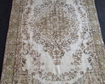 May include: A vintage rug with a cream background and a floral pattern in shades of brown and green. The rug has a border with a geometric design.
