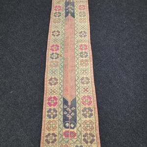 May include: A rectangular, vintage rug with a central peach-colored field and intricate floral and geometric patterns. The borders feature repeating floral motifs in shades of pink, blue, and green, with a dark blue and black central design.