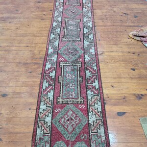 May include: A long, narrow rug with a traditional Turkish design. The rug is primarily red with white and green accents. The design features geometric shapes and floral motifs.