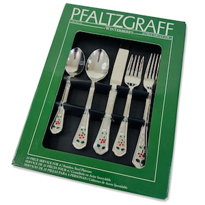 Puede incluir: Un juego de cubiertos de acero inoxidable Pfaltzgraff Winterberry de 20 piezas en una caja verde. El set incluye una cuchara, una cuchara sopera, un cuchillo y dos tenedores, cada uno con un diseño de acebo en el mango.