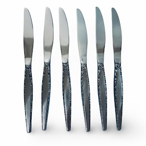 May include: A set of six stainless steel dinner knives arranged vertically. Each knife features a smooth, polished blade and a textured, brushed metal handle with a decorative border pattern along the edges of the handle.