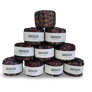 May include: A stack of ten yarn skeins. The yarn is a dark color with flecks of red, yellow, blue, and pink. Each skein has a white label with the word "GIOCO" printed in black. The yarn is distributed by KFI.
