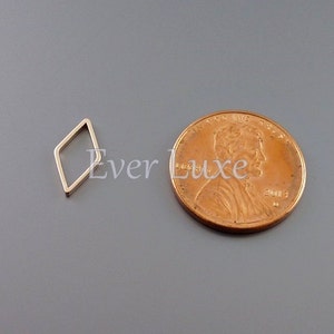 May include: A small, gold-colored, open diamond-shaped charm next to a penny. The charm is a simple geometric design, and the penny provides a size reference. The background is a solid gray.