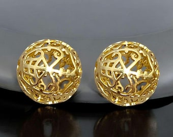 May include: A pair of gold-tone earrings with a delicate, intricate, and openwork design. The earrings are round and have a spherical shape.