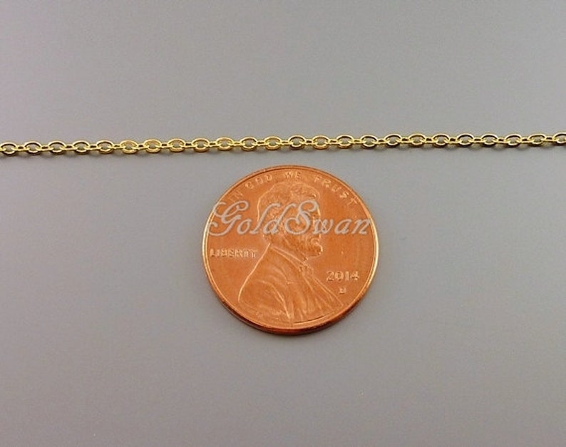 May include: A gold chain necklace next to a US penny for size comparison. The chain is made of small, oval-shaped links.