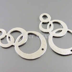 Peut inclure: Deux breloques d'oreille en métal argenté avec un motif de cercles qui se chevauchent. Les breloques ont une finition brossée et un trou en haut pour les attacher aux boucles d'oreilles.