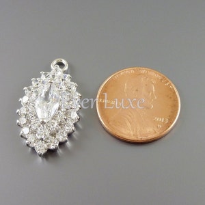 Puede incluir: Un colgante de plata con un gran cristal de imitaci&oacute;n transparente en forma de marquesa rodeado de cristales de imitaci&oacute;n m&aacute;s peque&ntilde;os. El colgante es aproximadamente del tama&ntilde;o de una moneda de un c&eacute;ntimo de euro.