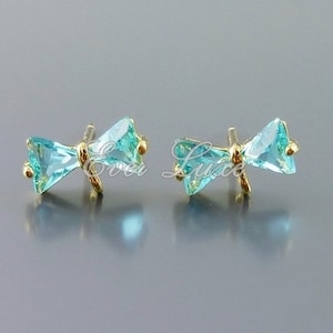 May include: A pair of gold bow-shaped earrings with light blue crystal accents.