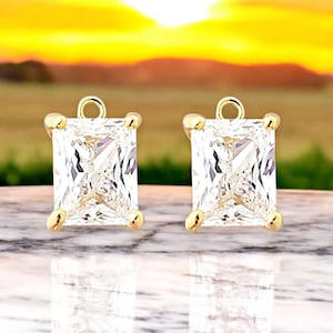 May include: A pair of gold earrings with square-shaped clear cubic zirconia stones.