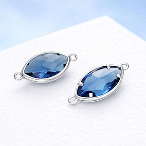 May include: Two marquise-shaped blue gemstone connectors with silver-colored metal settings. Each gem has a faceted surface and small loops on each end for attachment. The gems are a deep blue color.