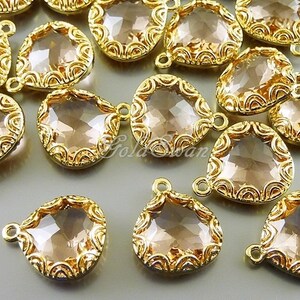 May include: A group of gold-tone teardrop-shaped pendants with clear glass stones. Each pendant has a delicate, ornate design around the edge.