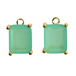 May include: Two square-shaped, mint-green gemstone charms with gold-colored accents. Each charm has a rectangular shape with rounded corners and a small loop at the top for attaching to jewelry. The corners are adorned with small gold-colored beads.