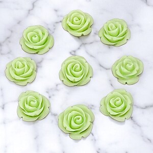 Op de afbeelding: Tien lichtgroene plastic rozenversieringen. De rozen hebben een diameter van ongeveer 2,5 cm en een 3D-ontwerp.