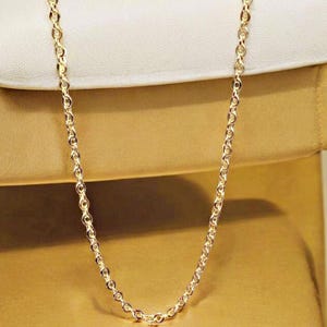 May include: A gold chain necklace with a delicate, round link design. The chain is displayed on a white and gold background.