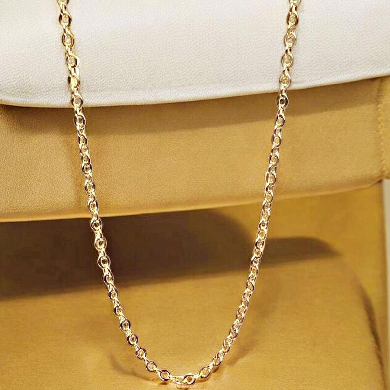 May include: A gold chain necklace with a delicate, round link design. The chain is displayed on a white and gold background.