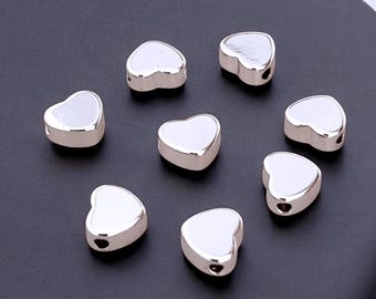 May include: Eight silver heart-shaped beads with a hole in the center. The beads are smooth and shiny.
