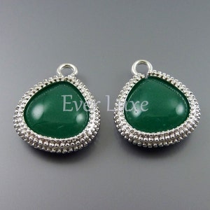 May include: A pair of silver teardrop-shaped earrings with a green stone in the center. The earrings have a beaded border.