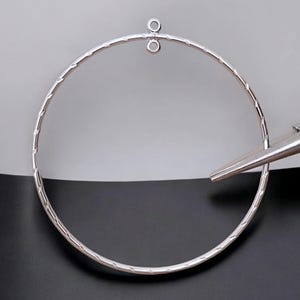 May include: A silver hoop earring with a textured surface and a jump ring at the top.