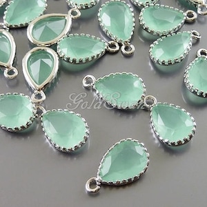 May include: A collection of light green teardrop-shaped glass pendants with silver-toned metal settings. The pendants have a scalloped edge and a loop at the top for attaching to jewelry.