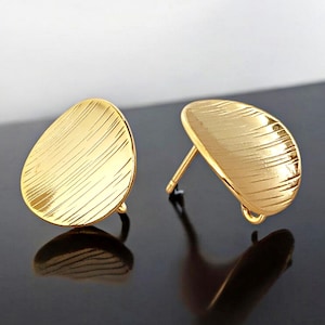 May include: A pair of gold-toned earrings with a textured, oval-shaped design. The earrings are made of metal and have a post-back closure.
