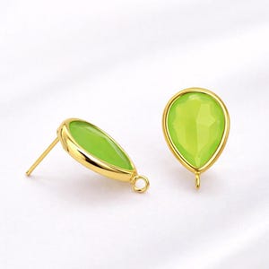 May include: A pair of gold-colored stud earrings with a pear-shaped, light green gemstone. The gemstones are set in a gold bezel setting. One earring is angled, showing the post and loop.