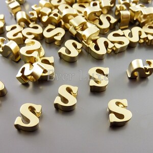 May include: A large pile of gold-colored letter 'S' beads. The beads are made of metal and have a shiny finish.