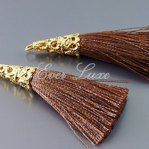 May include: Two brown silk tassels with gold metal caps. The caps have a decorative, intricate design.